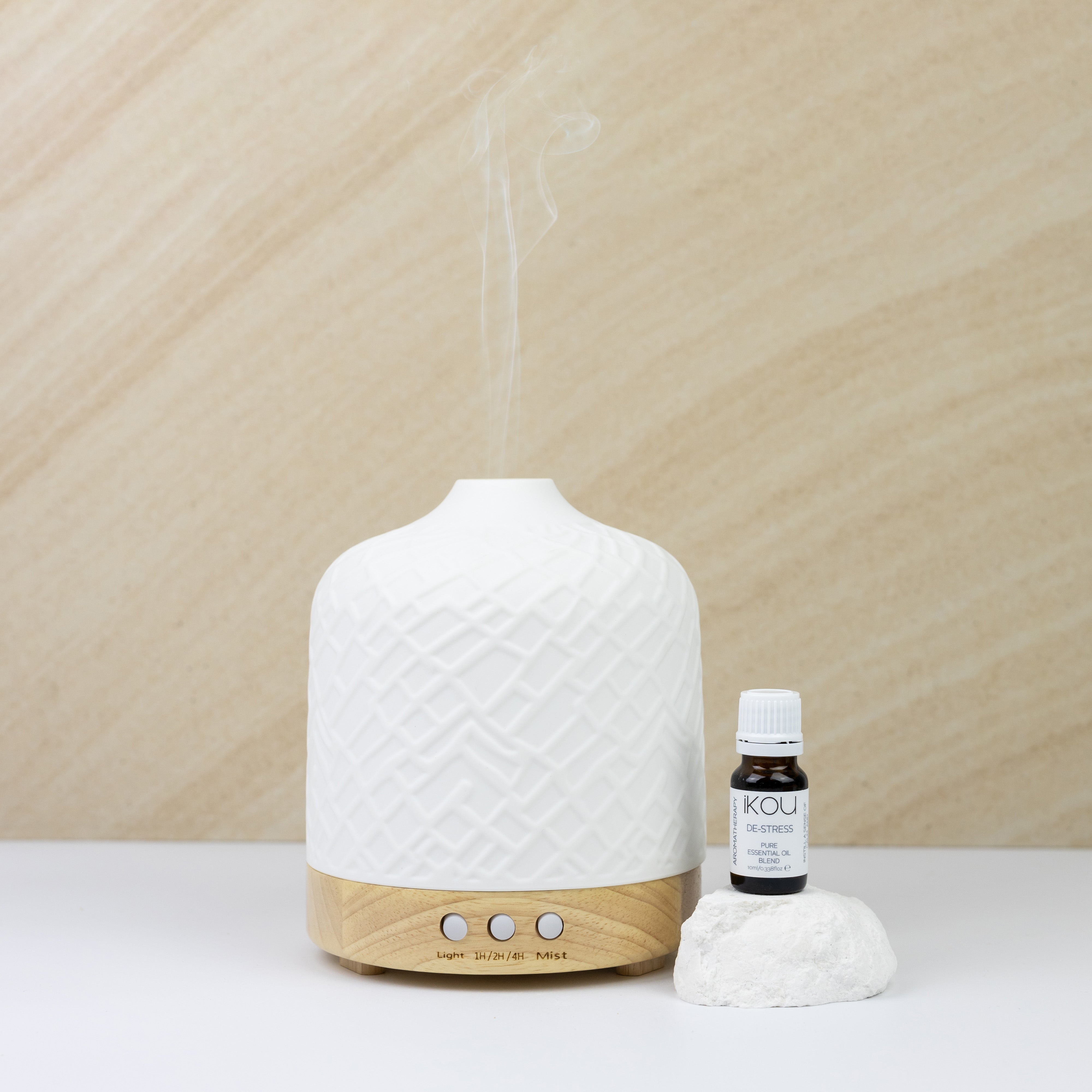 White textured diffuser with wooden base on a light surface, next to a small bottle of essential oil.