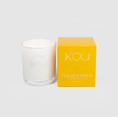 White candle in a clear glass holder next to a yellow box labeled 'KOU Golden Hour' on a light gray background