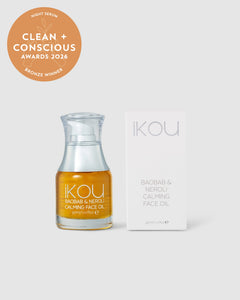 A bottle of iKOU Baobab & Neroli Calming Face Oil next to its white packaging box, with an bronze 'Clean + Conscious Awards 2026' badge in the top-left corner, set against a light grey background.