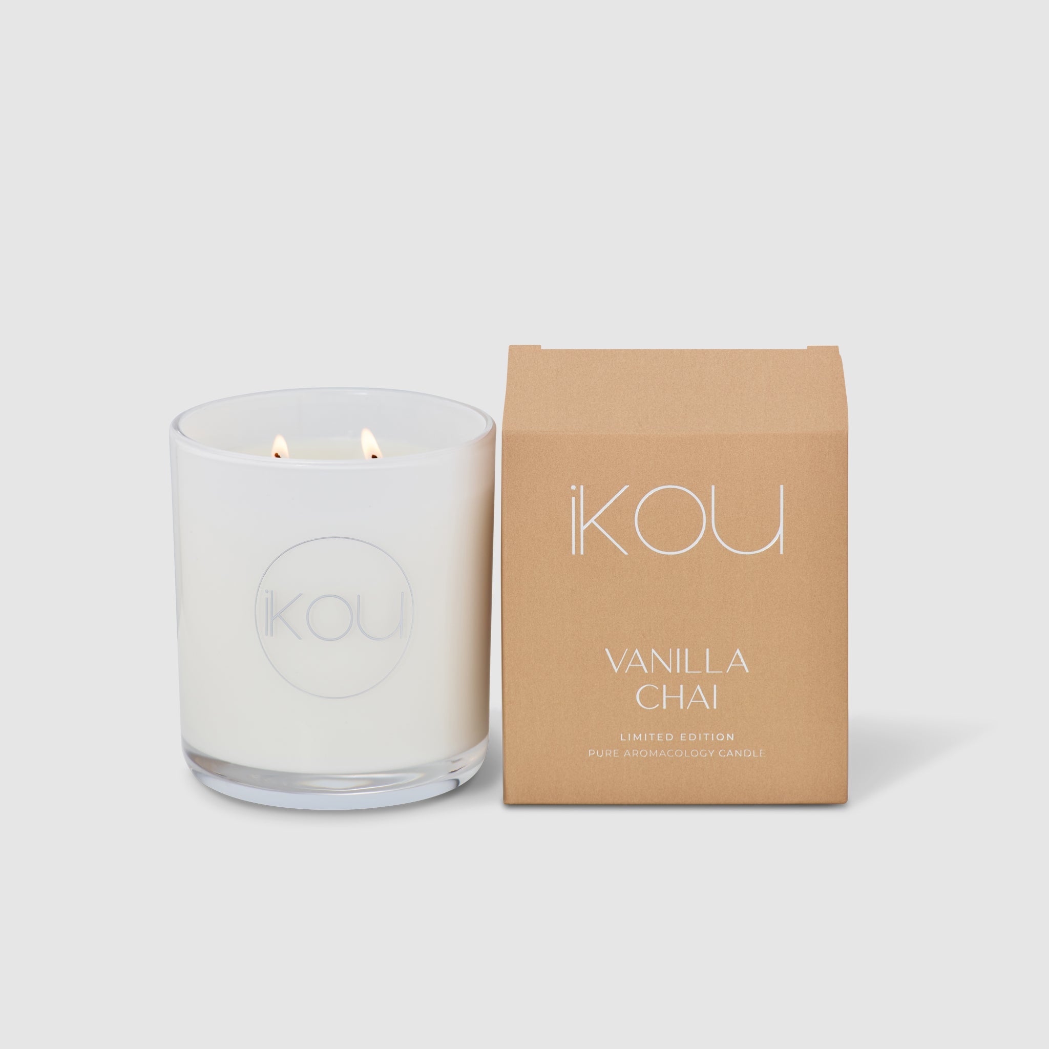 White candle with 'IKOU' branding next to a brown box labeled 'Vanilla Chai' on a white background