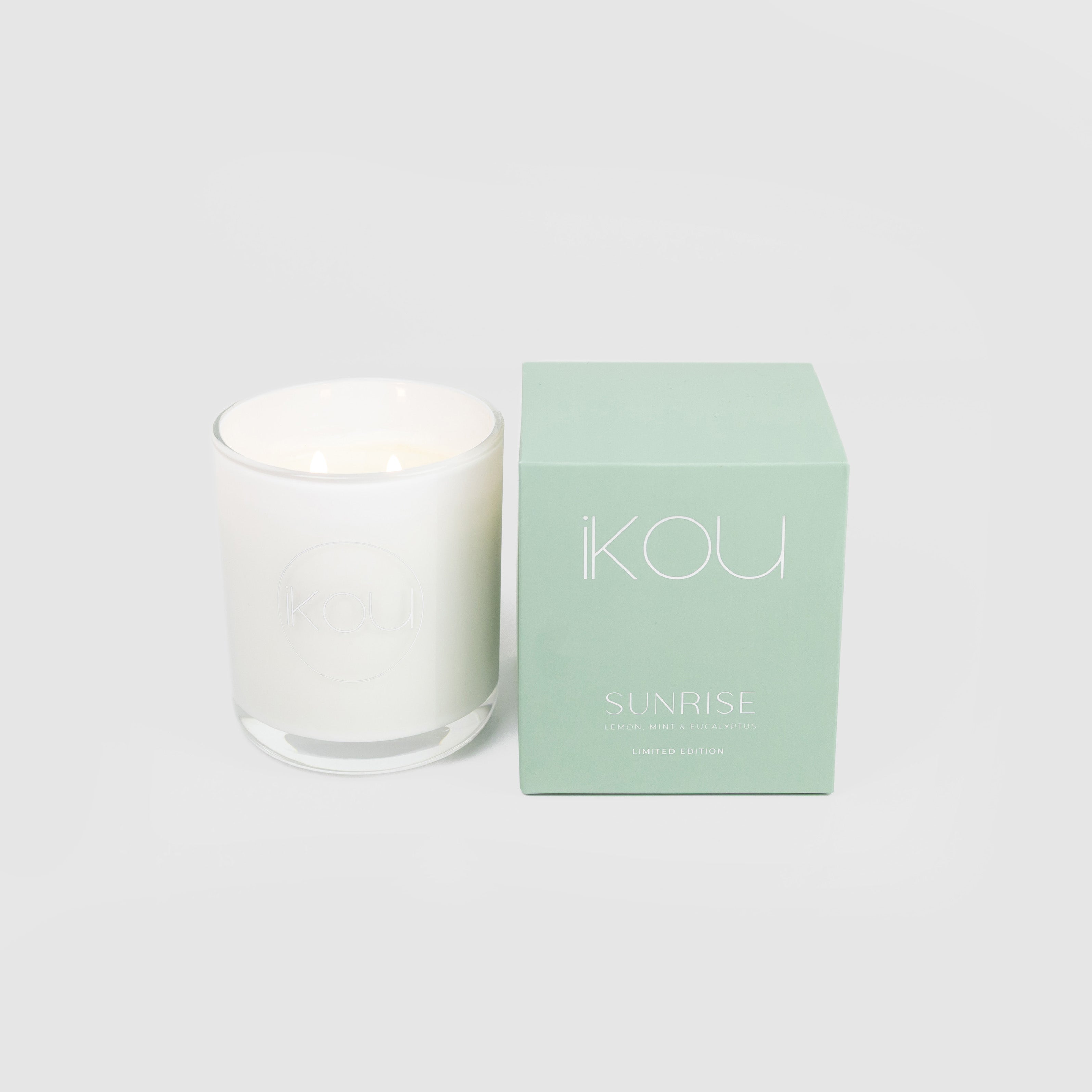 White candle with a green box labeled 'IKOU Sunrise' on a light gray background